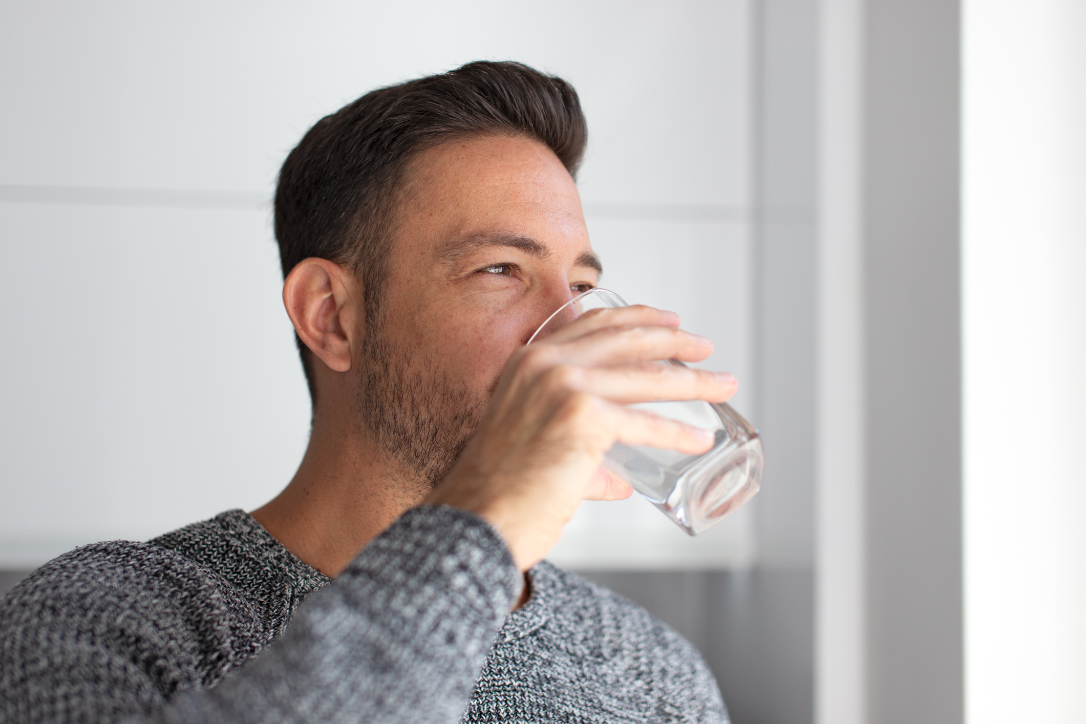 A man drinking water from a glass indoors.