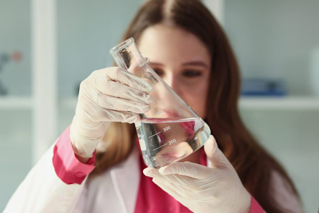 A young woman laboratory assistant examining a flask of water.