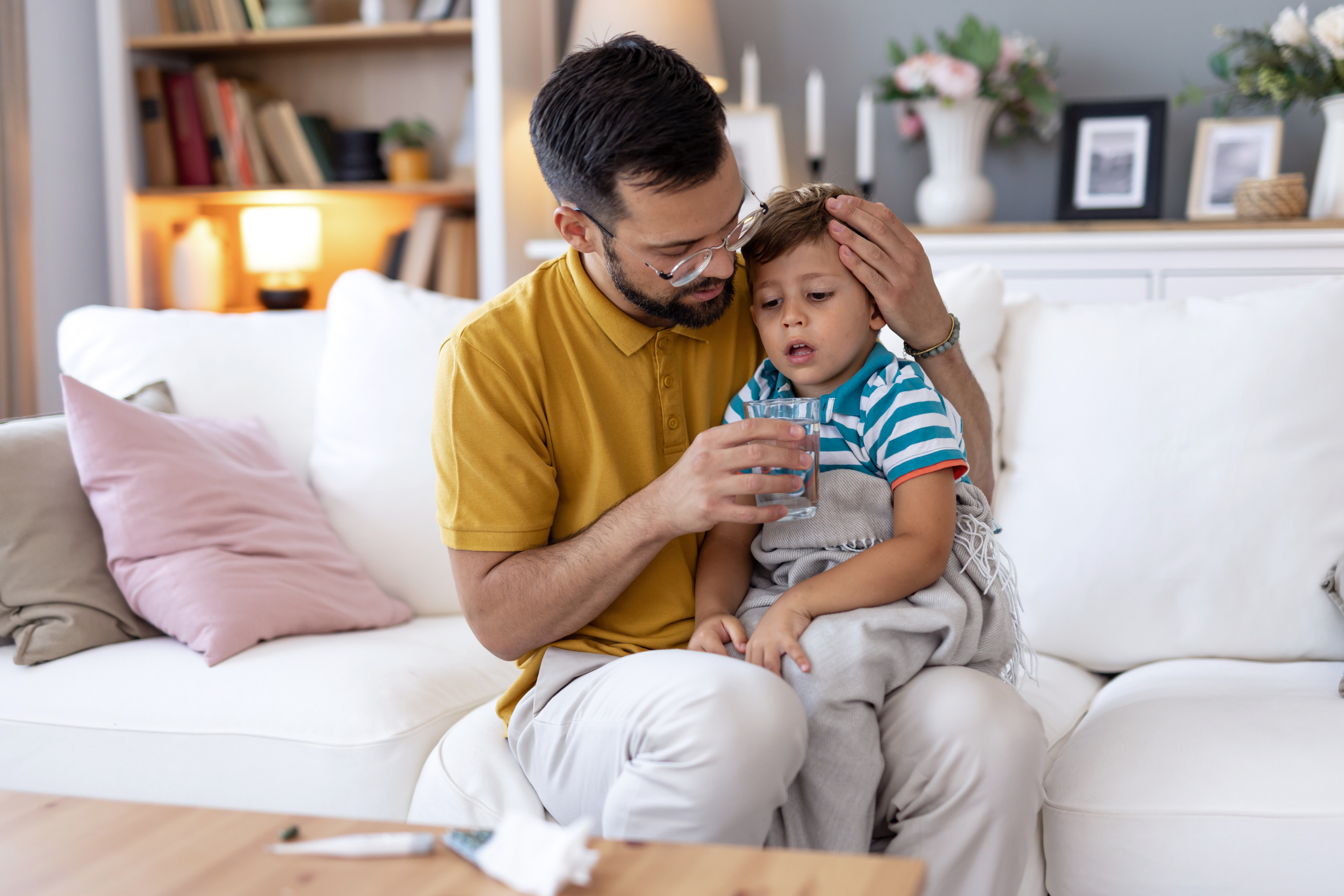 A father comforting a sick child with a glass of water.