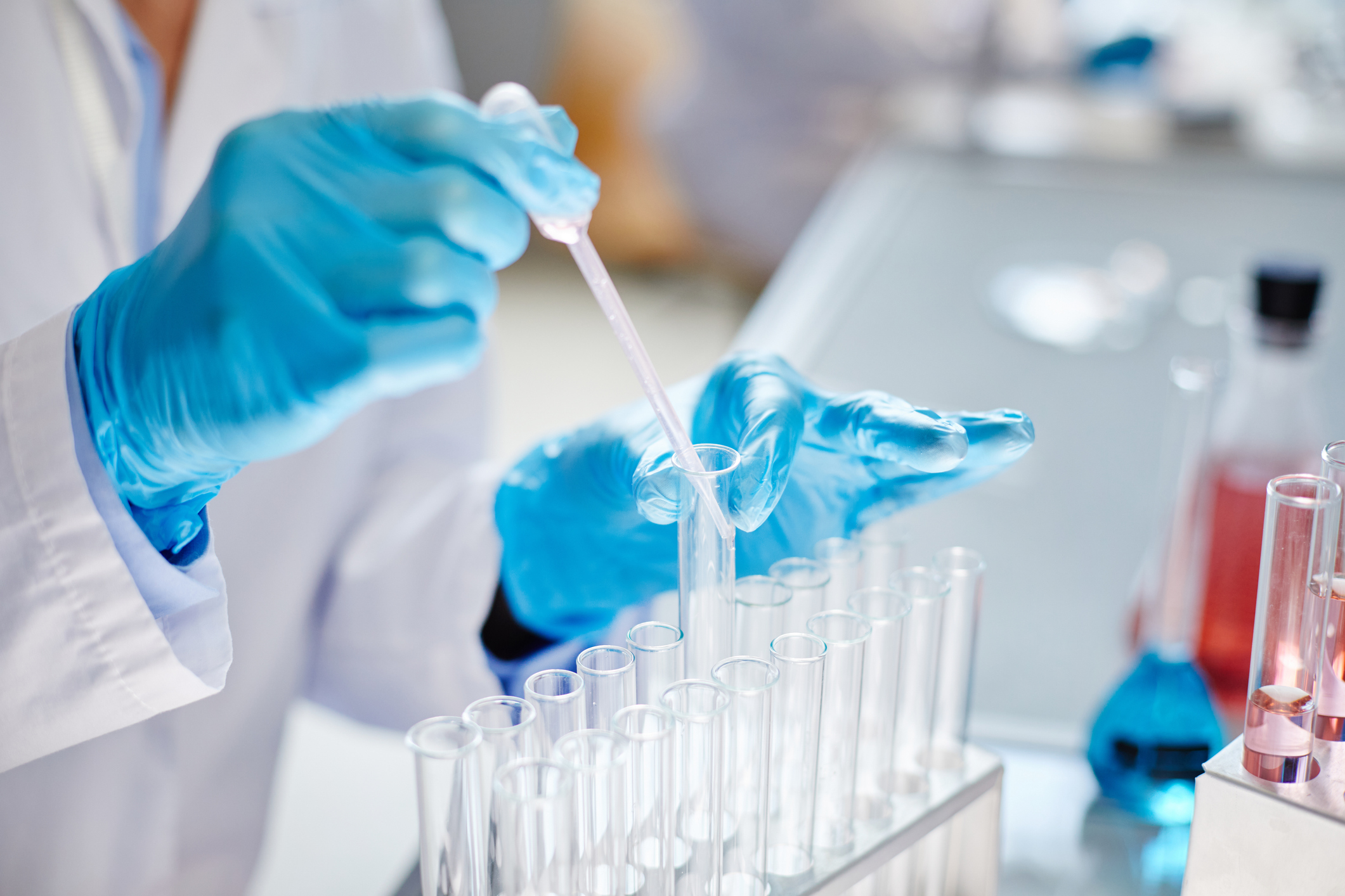 A scientist wearing blue gloves carefully uses a pipette to transfer liquid into a test tube in a laboratory setting.