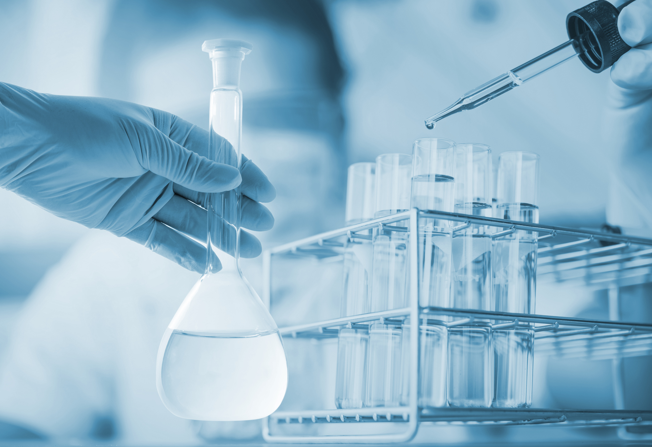 Scientist in a lab coat holding a flask with a water sample during laboratory testing.