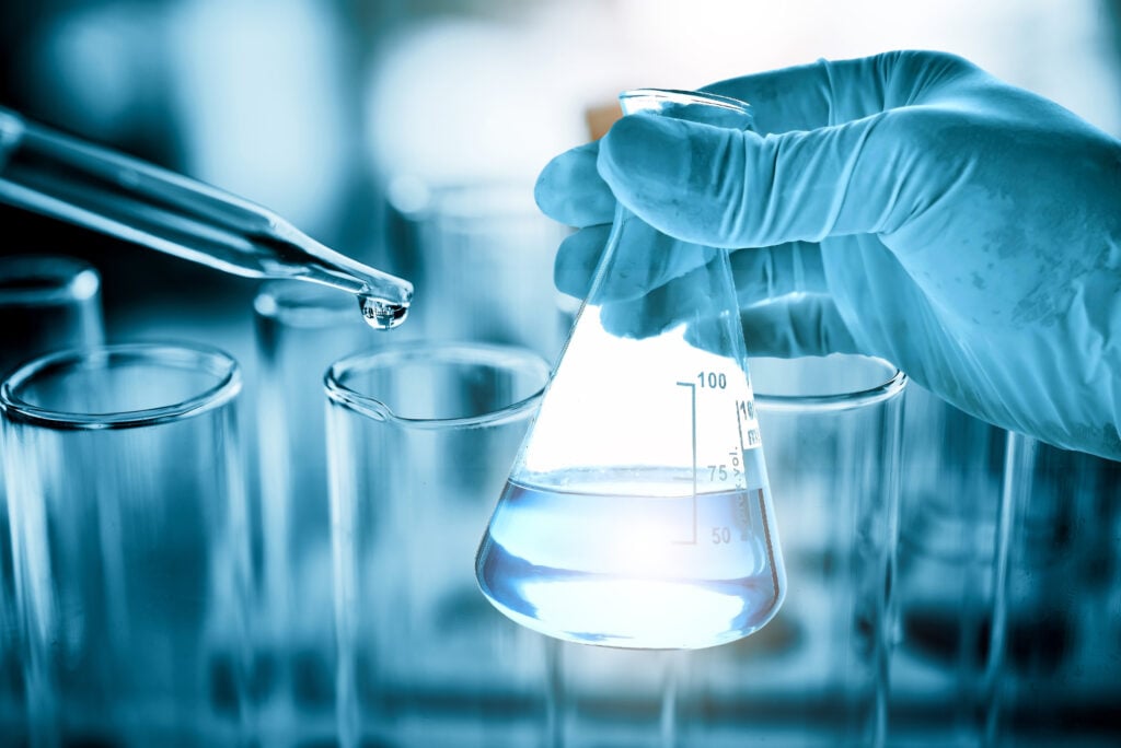Laboratory technician holding a flask and testing water quality in a laboratory setting.